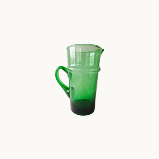 Hand-blown green glass pitcher with visible imperfections, adding charm to a rustic kitchen setting